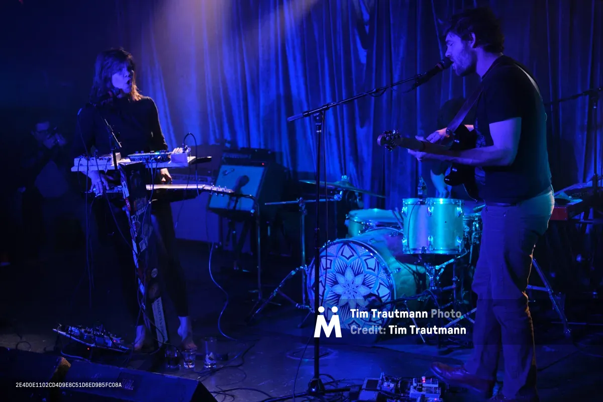 Experimental band Sun Blood Stories performs in the intimate confines of Dante's in downtown Portland during Rx Fest, bathed in deep cobalt stage lighting. The Boise-founded duo commands the small venue with synthesizers and drums, their silhouettes emerging from the moody blue atmosphere as theatrical curtains frame the performance. Electronic equipment and cables sprawl across the darkened stage, creating an authentic indie music scene captured in the heart of Portland's underground music culture.