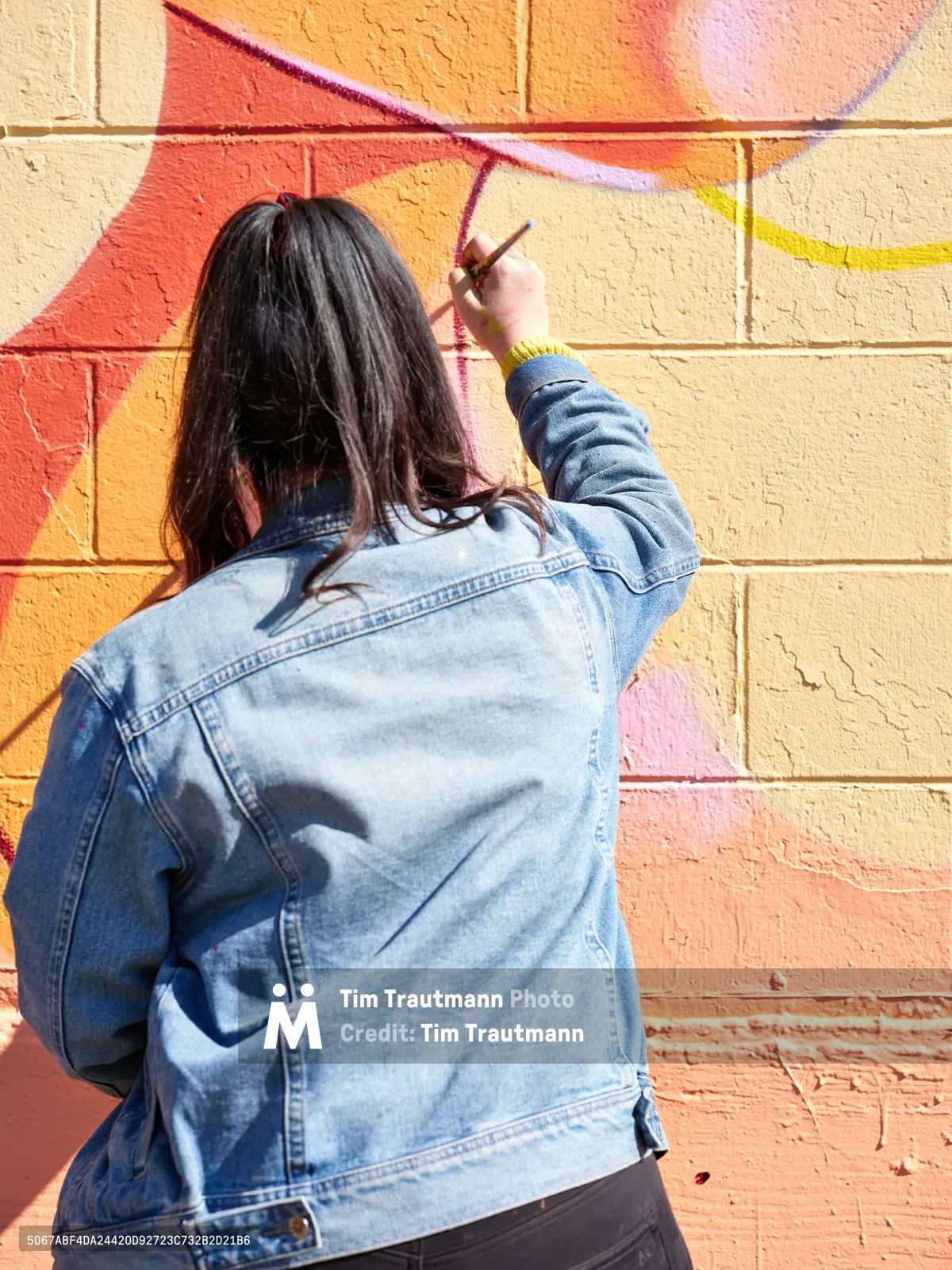 Multidisciplinary artist Vilatose works meticulously on her colorful mural 'Jardín Cubana' along Northeast Alberta Street in Portland's celebrated Alberta Arts District. Wearing a faded denim jacket with dark hair cascading down her back, she carefully applies paint to the textured brick wall, developing the three female figures that comprise the composition. The warm afternoon light illuminates both the artist and her vivid work-in-progress, capturing the creative energy that defines this historic neighborhood's artistic renaissance.