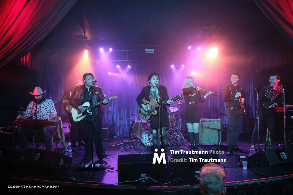 Six musicians of Roselit Bone perform under dramatic purple and amber stage lighting at Portland's iconic Dante's venue during RX Fest 2019. The intimate club setting frames the band with rich crimson curtains while atmospheric haze swirls through the colored beams, creating a moody backdrop for their eclectic instrumentation including guitars, violin, and keyboards. The low stage positioning places the audience at eye level with the performers, emphasizing the venue's legendary intimacy.