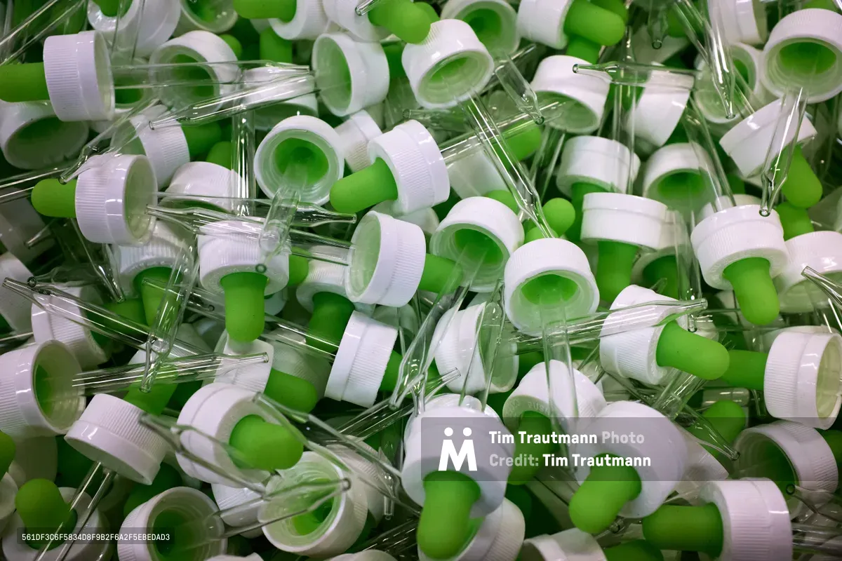 Hundreds of clear glass laboratory droppers with bright lime green rubber bulbs cascade in chaotic abundance across the frame. The pristine scientific instruments, photographed at SCRAP PDX in Portland's Goose Hollow neighborhood, create a mesmerizing pattern of transparency and vivid color. White plastic caps punctuate the composition, while the overlapping glass tubes catch and refract ambient light, transforming medical waste into an unexpected visual symphony of sustainability and creative potential.