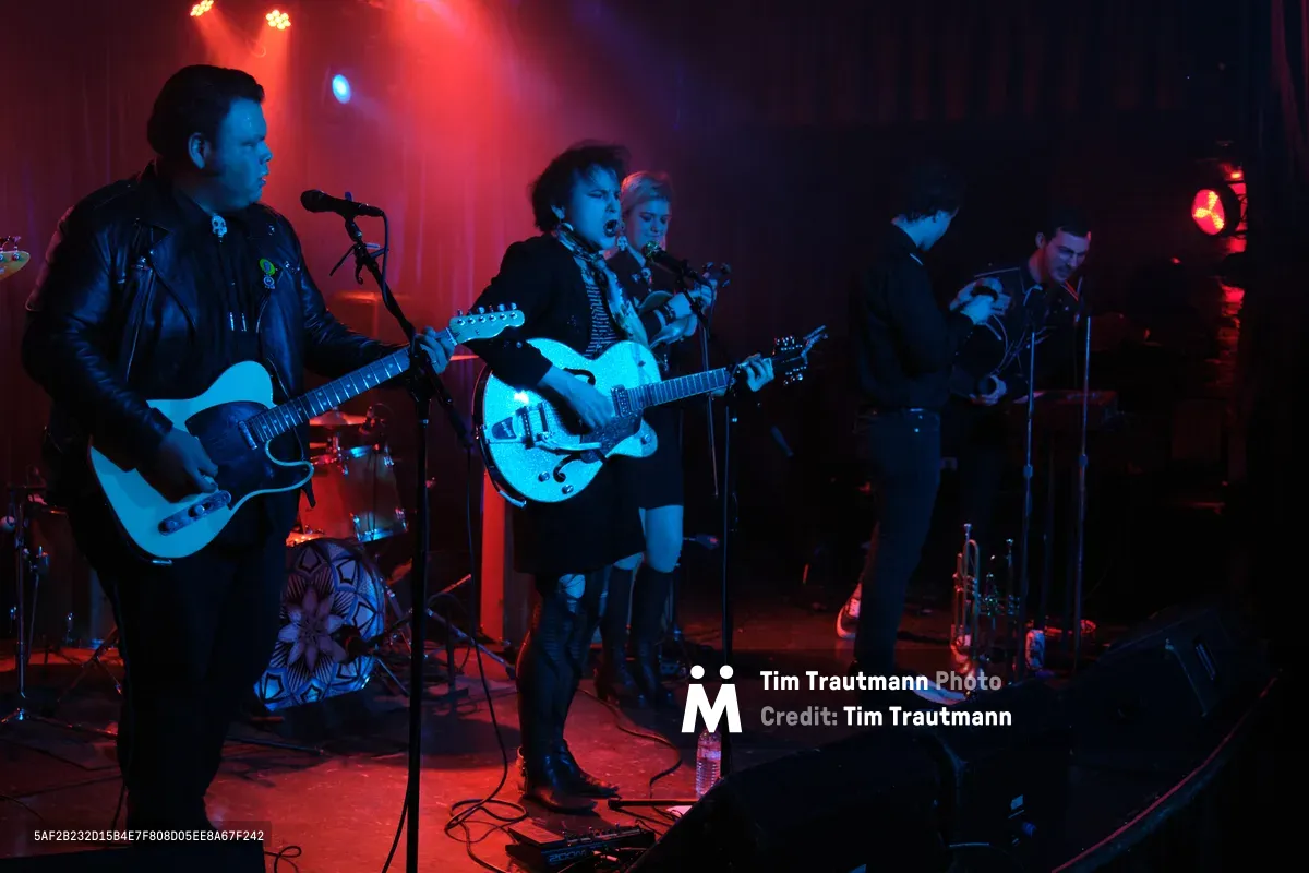 Victor Franco grips his Telecaster while Charlotte McCaslin commands center stage with her hollow-body guitar, Faith Grossnicklaus anchoring the rhythm section as Roselit Bone delivers an electrifying performance. The intimate venue pulses with crimson and azure stage lights, creating dramatic silhouettes against the smoky atmosphere of Portland's legendary Dante's. Microphone stands lean into the musical conversation while cables snake across the darkened stage, capturing the raw energy of RX Fest 2019.