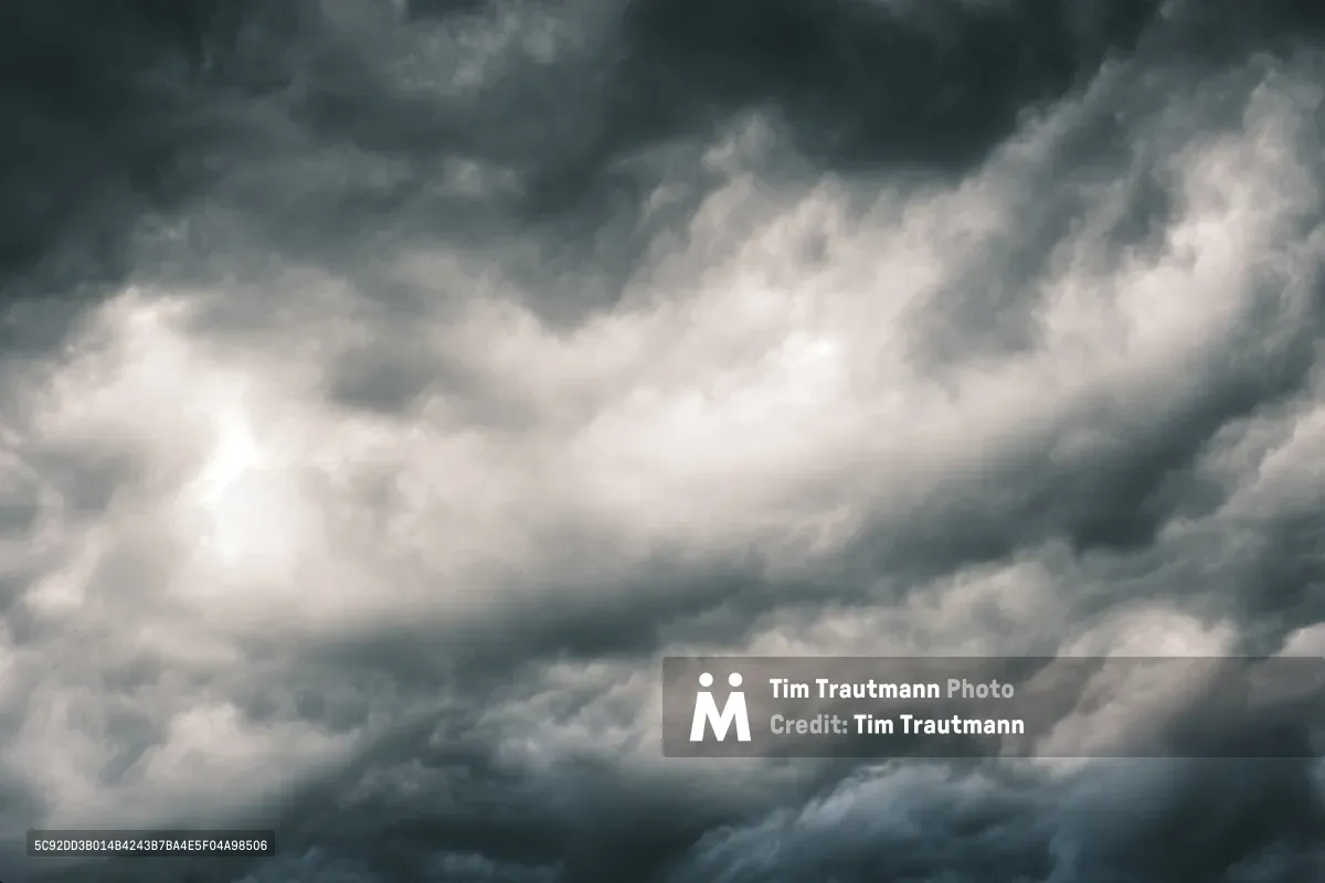 Dramatic cumulonimbus clouds billow across the Pacific Northwest sky above Irvington, Portland, their heavy gray masses pregnant with impending precipitation. The turbulent cloudscape creates a moody chiaroscuro effect, with brilliant white cloud peaks contrasting against the deep charcoal storm front rolling overhead. Soft diffused light filters through the atmospheric layers, casting the entire scene in muted tones that speak to Oregon's characteristic overcast weather patterns.