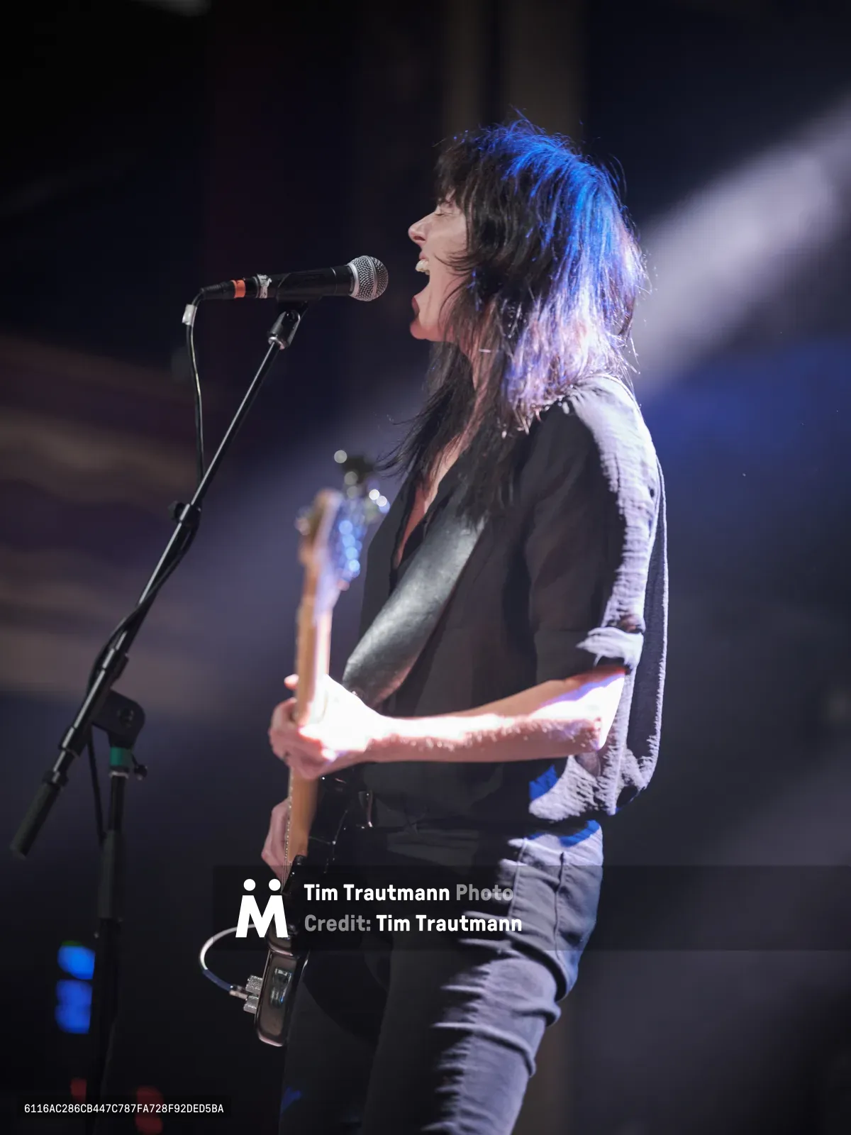 Emma Richardson of Band of Skulls delivers an intense vocal performance during the band's 10 Year Anniversary Tour at Webster Hall in Manhattan. Bathed in ethereal blue stage lighting, she leans into the microphone with raw emotion, her dark hair cascading as she grips her bass guitar. The dramatic lighting cuts through the venue's shadows, creating an intimate yet powerful moment that captures the essence of live rock performance.