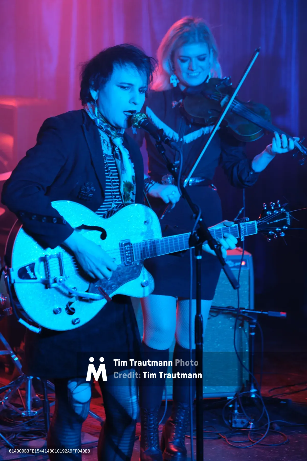 Charlotte McCaslin grips a white hollow-body guitar while Faith Grossnicklaus draws her violin bow in concentrated focus during Roselit Bone's performance at RX Fest 2019. Electric blue and magenta stage lighting bathes the duo in otherworldly hues against Dante's intimate club backdrop. The dramatic lighting transforms their black attire into silhouettes while highlighting the intensity of their musical connection, creating a moody atmosphere that captures the raw energy of Portland's underground music scene.