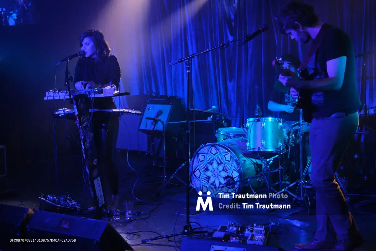 Experimental band Sun Blood Stories performs in the intimate, moody confines of Dante's in downtown Portland during Rx Fest. Electric blue stage lighting bathes the duo as the keyboardist leans into the microphone while the drummer maintains rhythm behind a geometric-patterned kit. The atmospheric lighting creates deep shadows against flowing curtains, capturing the mesmerizing sound of the Boise-founded band now based in Portland.