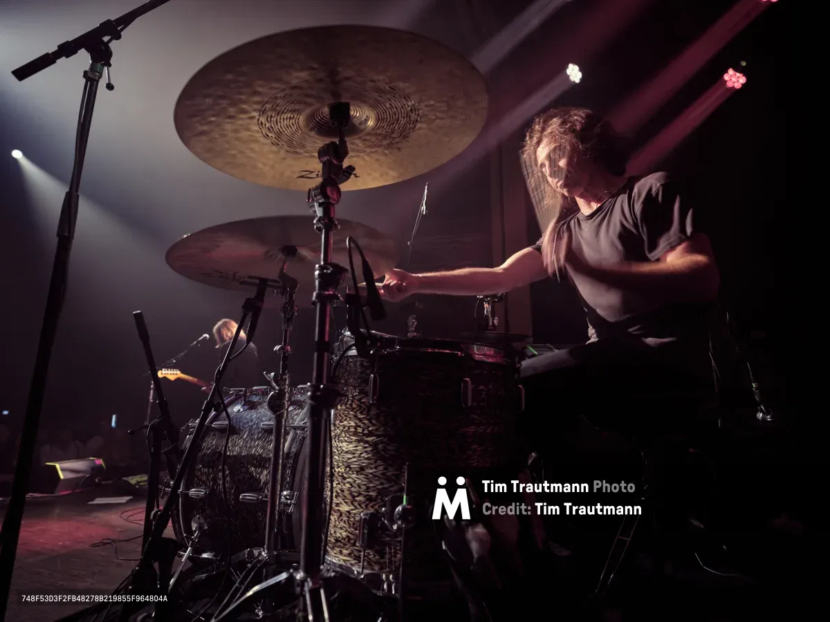 Drummer Julian Dorio of Band of Skulls unleashes rhythmic power behind his leopard-print kit during the band's 10 Year Anniversary Tour at Manhattan's historic Webster Hall. Stage lights carve dramatic shadows across his concentrated expression as he strikes cymbals suspended like bronze moons above the intricate hardware. The intimate venue's atmospheric lighting transforms the performance into a study of controlled intensity, capturing the percussive heartbeat that drives the English rock trio's decade-spanning catalog.