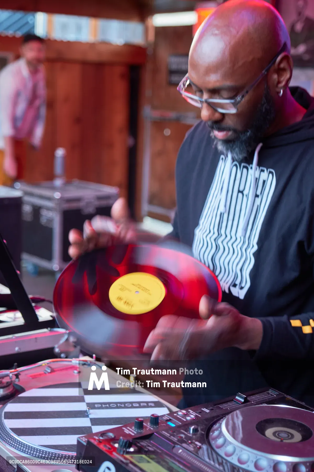 DJ Cee White commands the turntables at White Owl Social Club in Portland, his hands captured mid-motion as he manipulates a vibrant red vinyl record. The atmospheric lighting bathes the scene in warm amber and magenta hues, creating an intimate yet energetic ambiance typical of Portland's underground music venues. Motion blur on his hands emphasizes the kinetic energy of his performance, while the Pioneer DJ equipment gleams beneath the club's moody illumination. The photograph perfectly encapsulates the tactile artistry of vinyl DJing during this Sunday afternoon party opener.