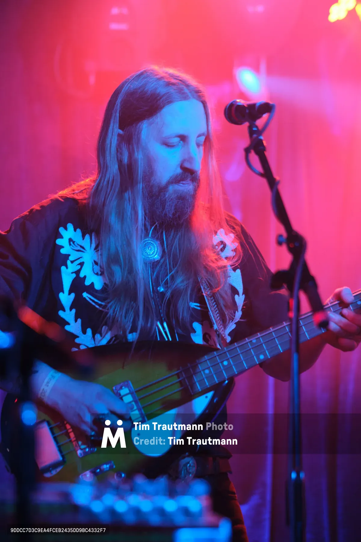 Tobias Berblinger of Roselit Bone lost in contemplative performance, his long blonde hair cascading as he cradles his bass guitar in the saturated magenta and blue stage lighting of Dante's. The intimate Portland venue's atmospheric haze creates a dreamlike backdrop, while ornate floral patterns on his dark shirt catch the vivid concert lighting. His downward gaze and gentle expression capture a moment of musical introspection during RX Fest 2019.