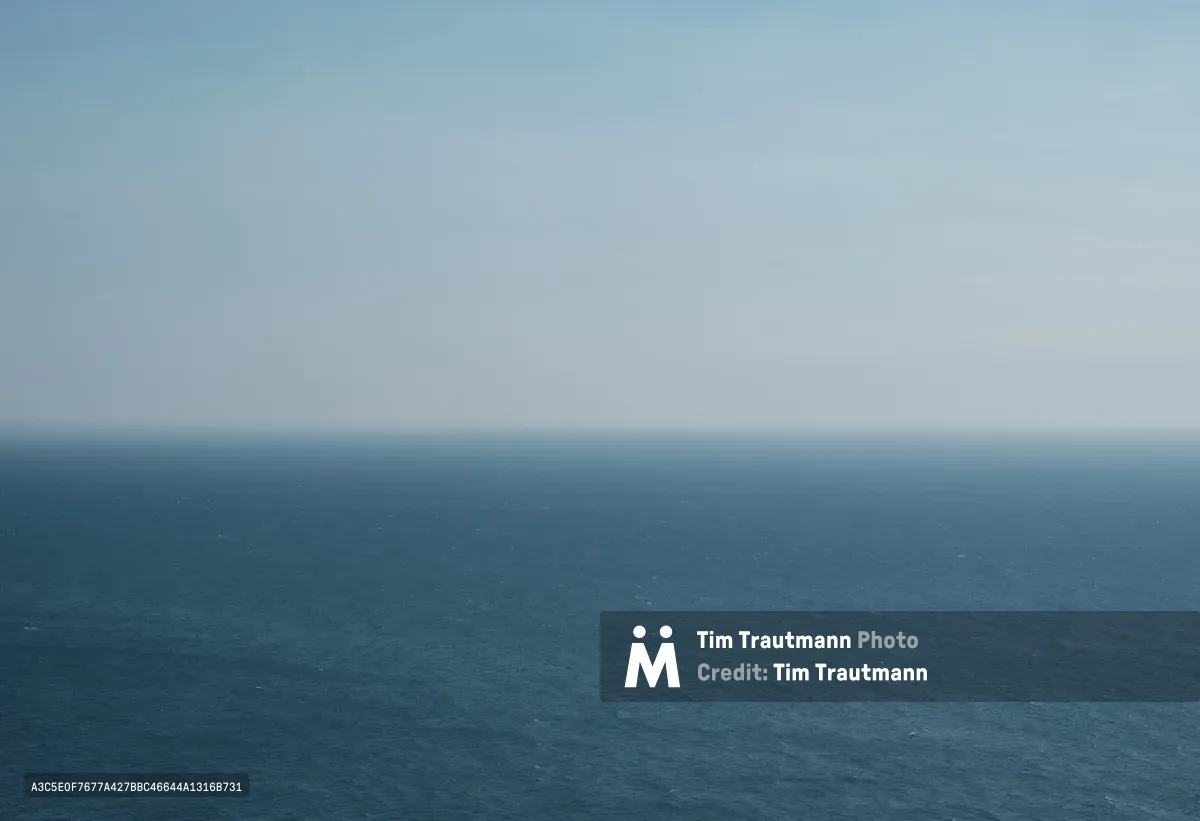 A minimalist seascape captures the infinite meeting of steel-blue Pacific waters and pale gray sky along the Oregon coastline. The horizon line divides the frame with mathematical precision, creating a meditative study in monochromatic blues and grays. Subtle texture in the ocean's surface hints at gentle swells, while the overcast sky maintains an ethereal, weightless quality typical of the Pacific Northwest's marine climate.
