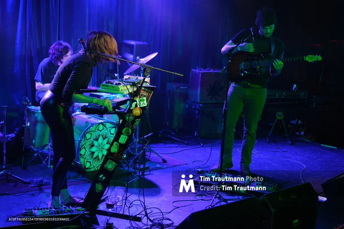 Sun Blood Stories delivers an intimate performance bathed in electric blue and green stage lighting at Dante's in downtown Portland. The keyboardist leans into their craft at center stage, flanked by intricate mandala artwork on their instrument, while the guitarist commands the right side of the frame. Cables snake across the wooden floor of this legendary venue, creating geometric patterns that mirror the psychedelic atmosphere of the underground music scene.