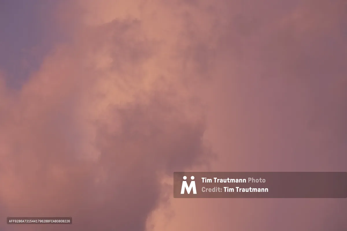 Soft cumulus clouds drift across a dusky sky painted in delicate shades of rose, lavender, and coral during evening hours over North Portland. The atmospheric conditions create a dreamlike canvas where warm peachy tones blend seamlessly with cooler purple hues, suggesting the tranquil moments of day's end. Wispy cloud formations catch and scatter the fading light, creating subtle variations in density and luminosity across the frame.
