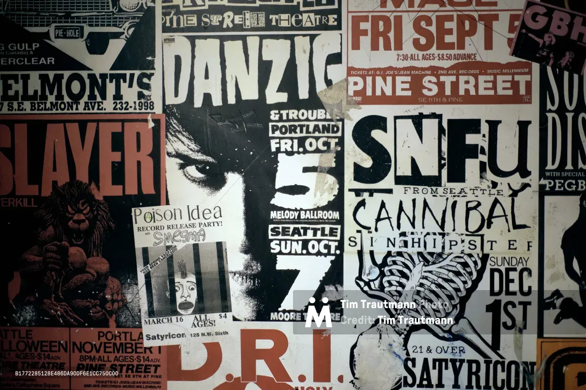 A dense collage of weathered concert promotional posters creates a visual archaeology of Portland's underground music culture. The overlapping flyers advertise performances by bands like Danzig, SNFU, and Cannibal at iconic venues including Pine Street Theatre and Satyricon. Muted earth tones and stark black-and-white graphics tell the story of the city's gritty alternative music heritage through torn paper and faded ink.