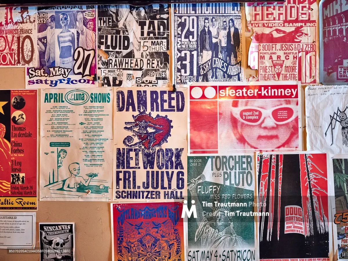 A densely layered collage of weathered concert posters and flyers creates a visual time capsule of Portland's indie music scene on the wall of Foster Burger. The overlapping promotional materials showcase bands like Dan Reed Network, Sleater-Kinney, and various underground acts, their faded colors and torn edges telling stories of late-night shows at venues like La Luna and Satyricon. The chaotic arrangement pulses with the raw energy of DIY concert promotion, each poster a artifact of the city's vibrant cultural underground.