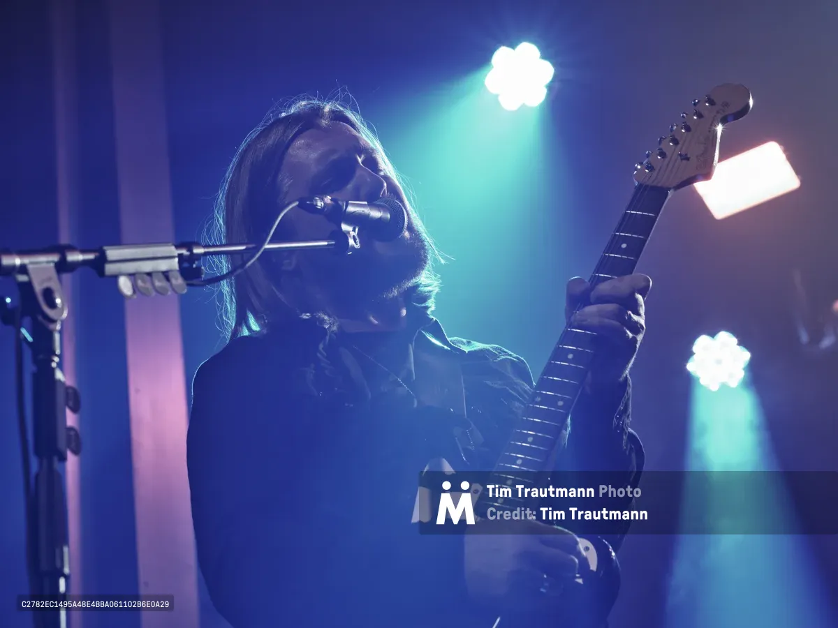 Russell Marsden of Band of Skulls delivers an electrifying performance at Webster Hall during the band's 10 Year Anniversary Tour. Bathed in ethereal blue and cyan stage lighting, the guitarist-vocalist leans into his microphone while gripping his electric guitar, his shoulder-length hair catching the atmospheric glow. The intimate venue's lighting creates a dreamy haze around the performer, capturing the raw energy and nostalgic celebration of a decade-long musical journey in Manhattan's historic music district.