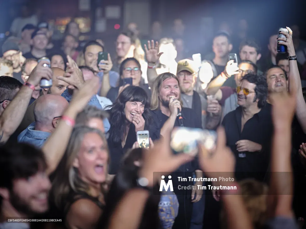 Emma Richardson and Russell Marsden of Band of Skulls are engulfed by an ecstatic crowd during their 10 Year Anniversary Tour at Manhattan's legendary Webster Hall. The intimate venue pulses with euphoric energy as fans raise smartphones and drinks toward the performers, creating a sea of illuminated faces bathed in atmospheric stage lighting. The smoky haze and tightly packed audience capture the raw intensity of live rock performance in one of New York's most storied music venues.