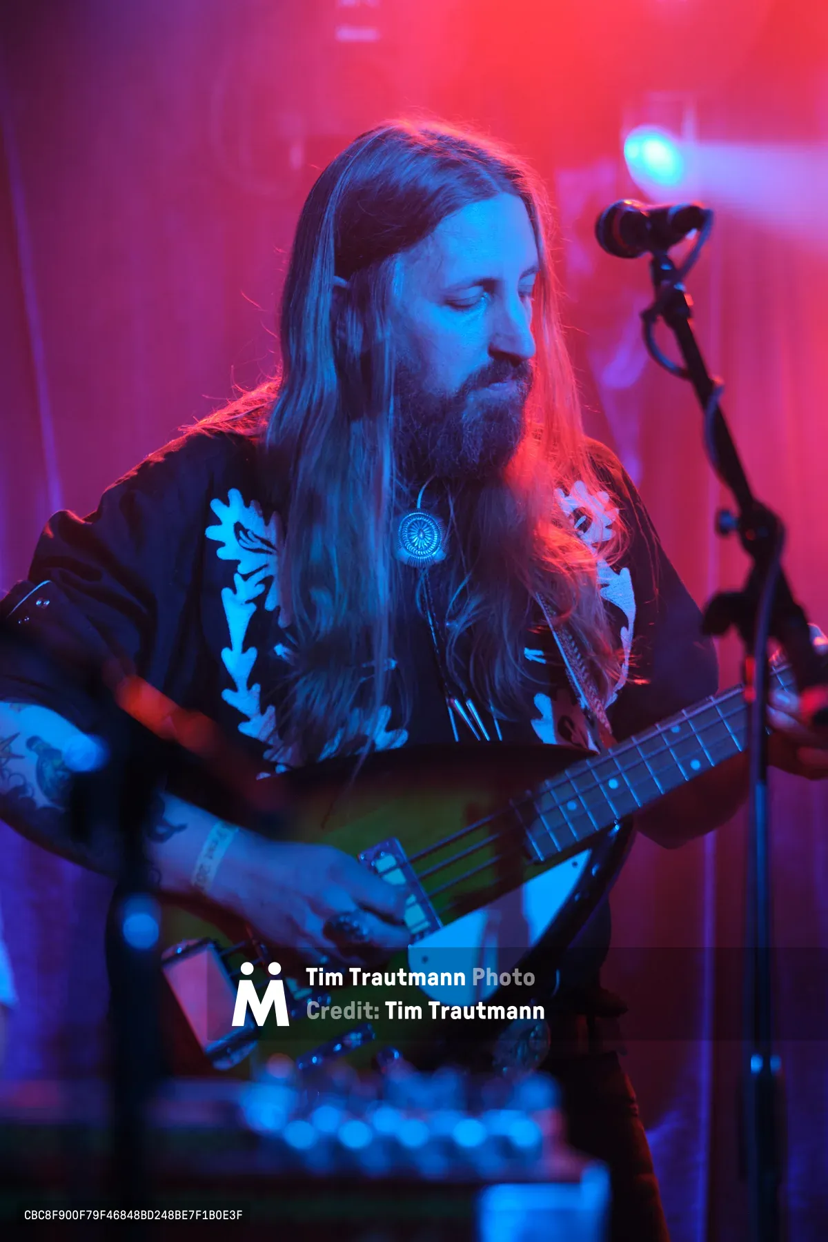 Tobias Berblinger of Roselit Bone surrenders to the sonic ritual beneath Dante's crimson-soaked stage lights in Portland. His flowing hair catches the electric blue and magenta wash as he cradles his bass guitar, eyes closed in musical meditation. The intimate venue pulses with atmospheric haze while his floral-printed shirt becomes a canvas for the club's signature neon palette. This moment captures the raw spirituality of underground performance, where musician and audience dissolve into pure sound.