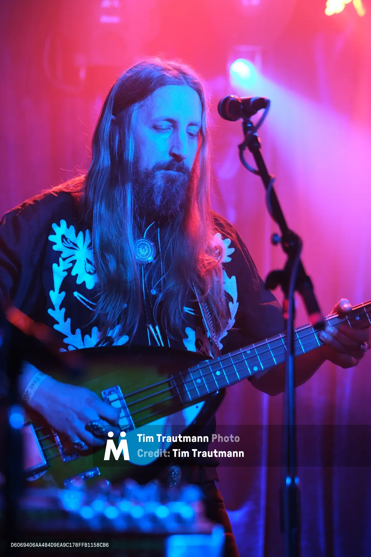 Tobias Berblinger of Roselit Bone commands the stage in a wash of electric blue and magenta lighting at RX Fest 2019. His long hair cascades over a floral-patterned shirt as he leans into his bass guitar, eyes closed in musical concentration. The intimate venue atmosphere is thick with colored stage lights cutting through atmospheric haze, creating a dreamlike quality that captures the raw energy of Portland's underground music scene.