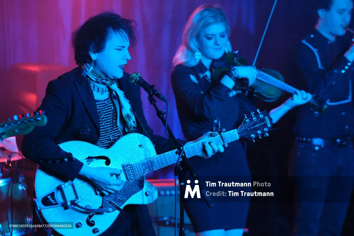 Charlotte McCaslin commands the foreground with her pristine white hollow-body guitar, singing into the microphone while bathed in electric blue stage lighting. Behind her, Faith Grossnicklaus draws her violin bow across the strings, both musicians absorbed in their performance at the intimate Dante's venue. The atmospheric lighting creates a dreamlike quality, with deep purples and blues washing over the duo as they deliver their ethereal sound to the RX Fest 2019 audience. The composition captures the intimate yet electric energy of live performance in Portland's renowned underground music scene.