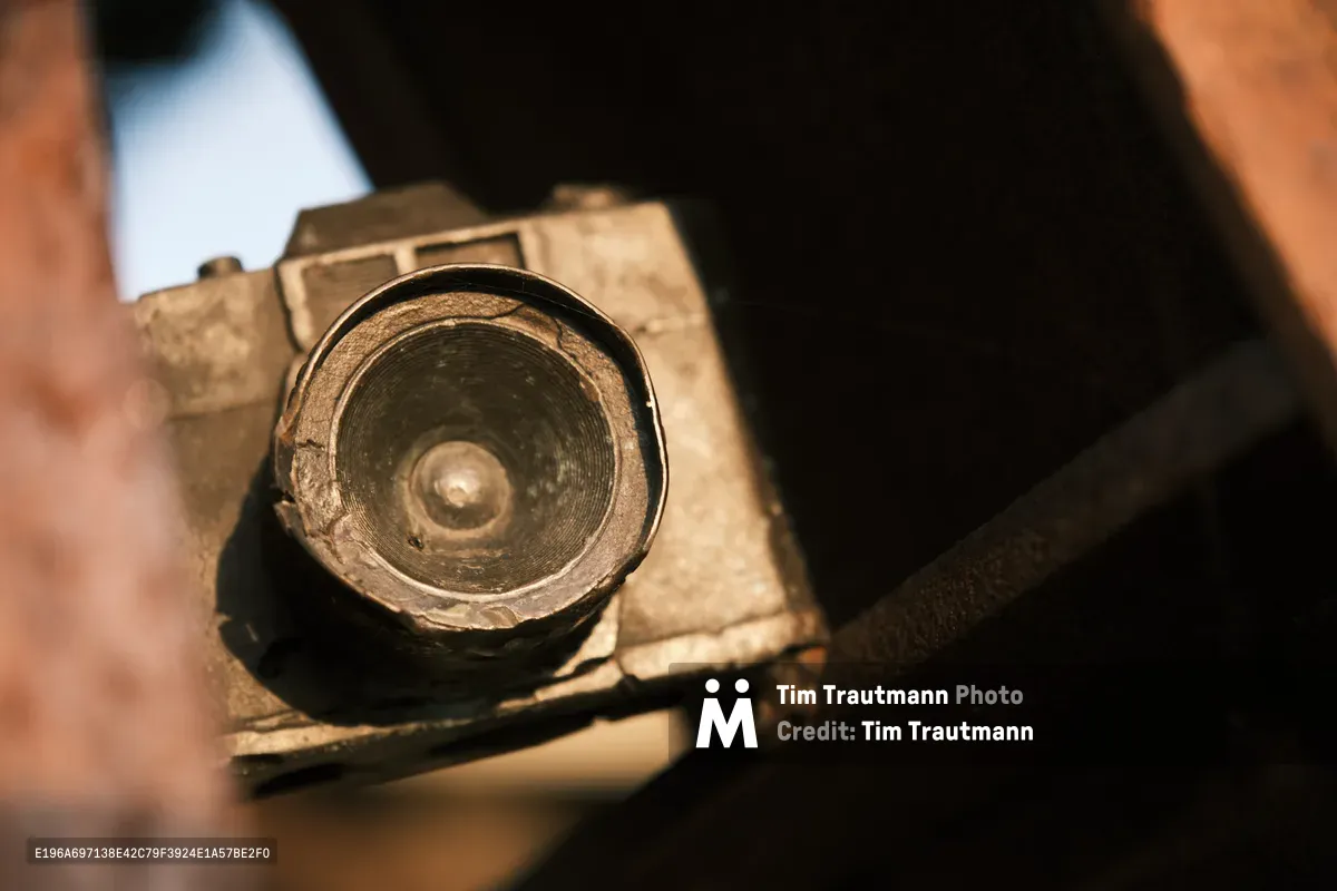 A weathered vintage camera lens rests in gentle hands within Portland's historic Skidmore district, its brass elements catching warm afternoon light. The intimate close-up reveals the circular glass element and aged metal housing, suggesting decades of photographic storytelling. Soft shadows and golden tones create an atmosphere of reverence for analog craftsmanship and photographic heritage.