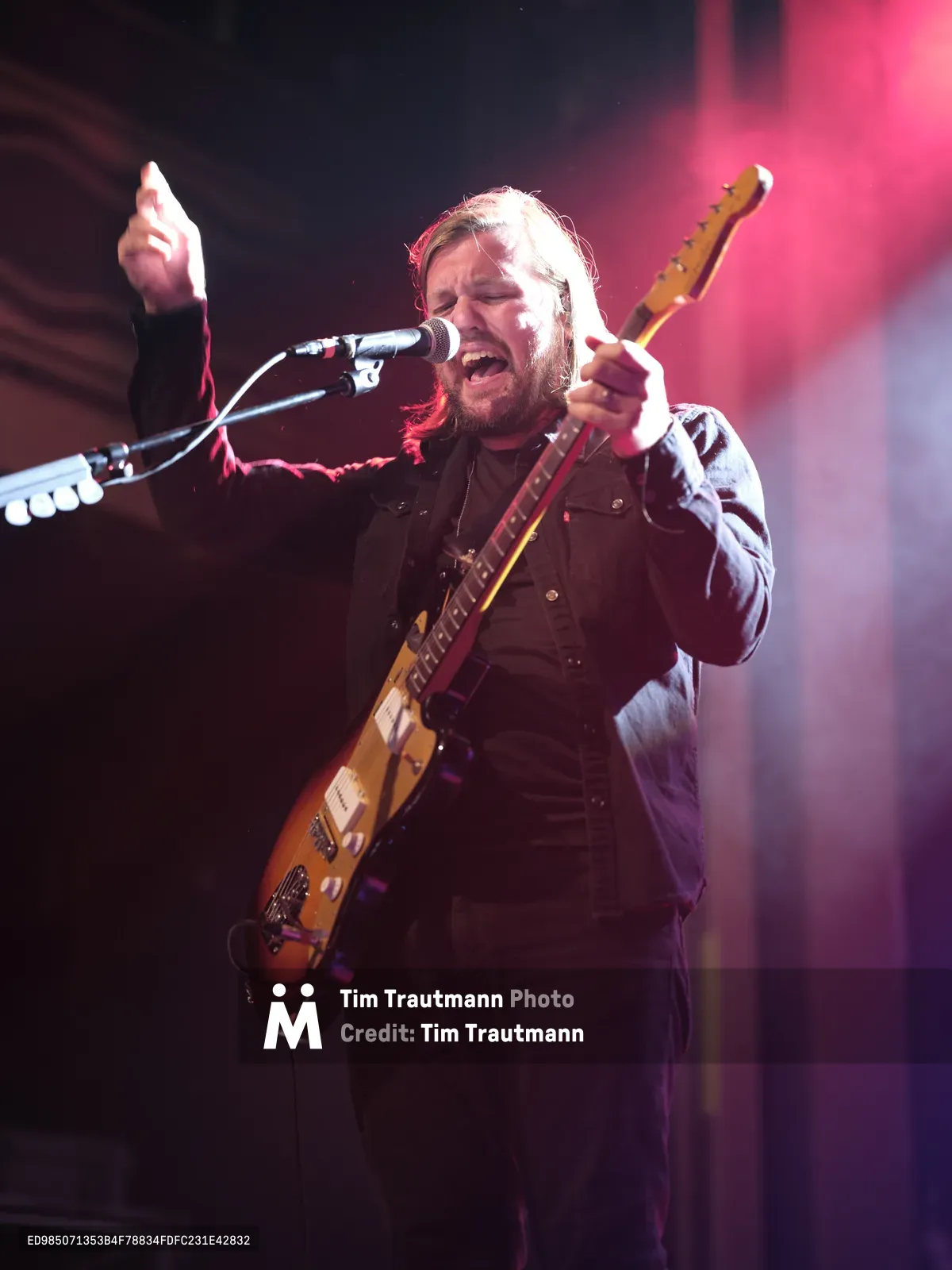 Russell Marsden of Band of Skulls commands the stage at Webster Hall during their 10 Year Anniversary Tour, his weathered Telecaster gleaming under magenta stage lights. The bearded frontman's passionate vocals and raised fist capture the raw intensity of live rock performance. Atmospheric smoke and dramatic lighting create a moody backdrop against the historic Manhattan venue's dark interior, while his focused expression reveals the emotional depth of the moment.