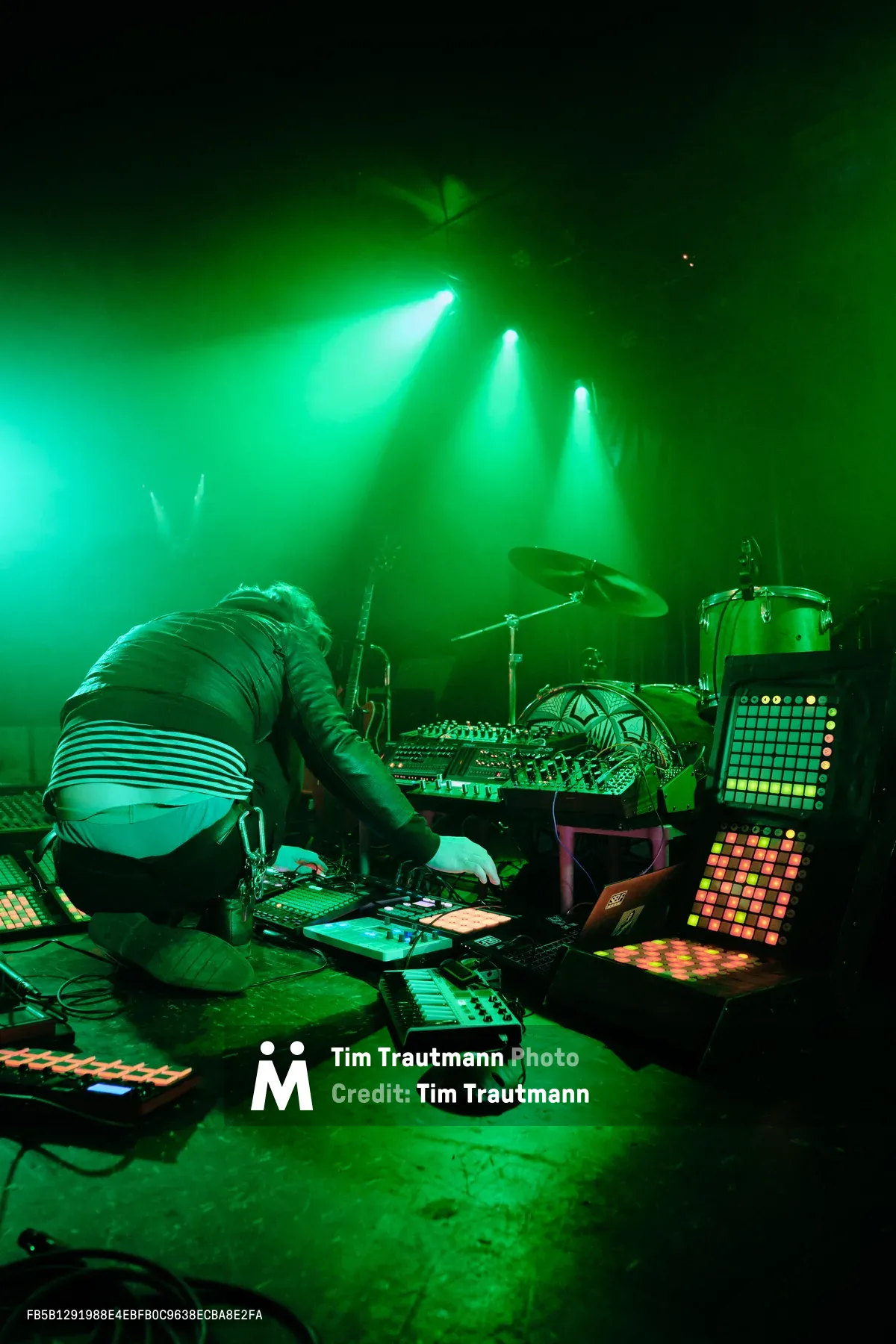 Electronic musician Eli Savage performs as Ellipsism at RX Fest 2019, hunched over an intricate array of synthesizers and drum machines at Portland's iconic Dante's venue. Piercing emerald spotlights cut through the smoke-filled darkness, casting an otherworldly glow over the densely packed performance setup. The artist's silhouette disappears into the maze of glowing control panels and grid controllers that sprawl across the stage floor, creating an immersive sonic laboratory bathed in electric green luminescence.