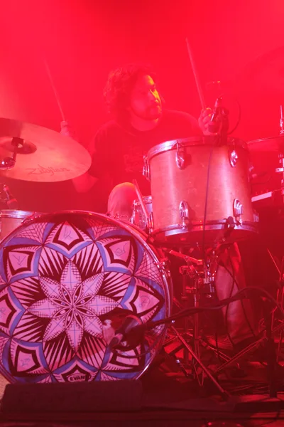 A drummer from Sun Blood Stories performs behind an ornate mandala-patterned kick drum, bathed in deep red stage lighting at Dante's in downtown Portland. The atmospheric lighting transforms the drum kit into a ceremonial altar, with intricate geometric patterns on the bass drum creating a mystical focal point. Cymbal stands rise like incense through the saturated crimson haze, while the performer remains partially obscured in the theatrical ambiance.
