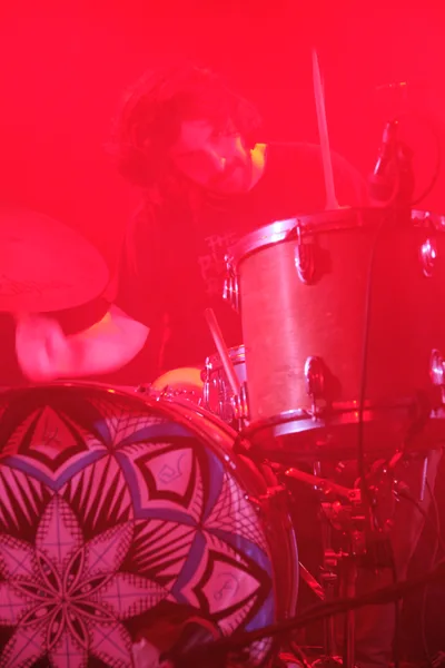 A drummer from experimental band Sun Blood Stories performs behind a drum kit awash in deep red stage lighting at Dante's venue in downtown Portland. The intense crimson wash creates an ethereal, almost otherworldly atmosphere, transforming the geometric patterns on the drum kit into shadowy mandala-like designs. Steam or haze drifts through the saturated light, while the musician remains a silhouetted figure within this scarlet-soaked sonic landscape.