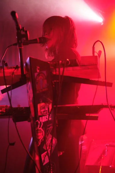 A keyboardist from Sun Blood Stories becomes silhouetted against a dramatic wash of crimson and magenta stage lighting at Dante's in downtown Portland. The performer's blonde hair catches the ethereal glow while they lean into their instrument, surrounded by synthesizer equipment and microphone stands. The atmospheric lighting transforms the intimate venue into a dreamlike sonic landscape, with deep reds bleeding into purple shadows.