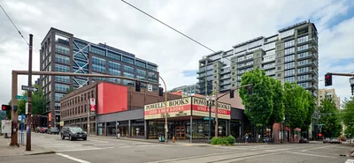 The iconic Powell's City of Books stands eerily quiet at the intersection of West Burnside Street in Portland's Pearl District during the COVID-19 pandemic lockdown of May 2020. The legendary bookstore's familiar corner location, with its distinctive red and cream facade, sits empty beneath overcast skies while modern residential towers loom behind. Traffic lights cast their colored glow over nearly deserted streets, creating a haunting portrait of urban isolation during one of the city's most challenging periods.