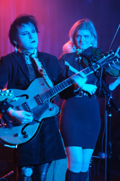 Charlotte McCaslin and Faith Grossnicklaus of Roselit Bone command the stage at Dante's in Portland, bathed in electric blue and magenta light. McCaslin's white hollow-body guitar gleams under the theatrical lighting while Grossnicklaus draws her violin bow with focused intensity. The atmospheric haze and saturated color wash transforms the intimate venue into a dreamlike sonic landscape, capturing the duo's genre-blending artistry in full flight.