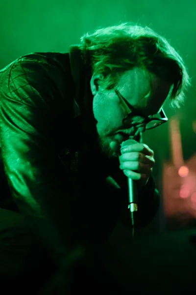 Electronic musician Eli Savage of ellipsism performs in a wash of ethereal green stage lighting at Dante's venue in Portland, Oregon. The artist leans into the microphone with concentrated intensity, his wire-rimmed glasses catching the ambient glow while tousled hair frames his focused expression. The moody emerald illumination creates an otherworldly atmosphere, transforming the intimate downtown venue into a sonic sanctuary.