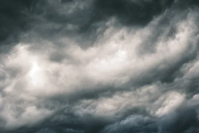 Dramatic cumulonimbus clouds billow across the Pacific Northwest sky above Irvington, Portland, their heavy gray masses pregnant with impending precipitation. The turbulent cloudscape creates a moody chiaroscuro effect, with brilliant white cloud peaks contrasting against the deep charcoal storm front rolling overhead. Soft diffused light filters through the atmospheric layers, casting the entire scene in muted tones that speak to Oregon's characteristic overcast weather patterns.