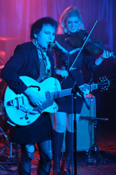 Charlotte McCaslin grips a white hollow-body guitar while Faith Grossnicklaus draws her violin bow in concentrated focus during Roselit Bone's performance at RX Fest 2019. Electric blue and magenta stage lighting bathes the duo in otherworldly hues against Dante's intimate club backdrop. The dramatic lighting transforms their black attire into silhouettes while highlighting the intensity of their musical connection, creating a moody atmosphere that captures the raw energy of Portland's underground music scene.