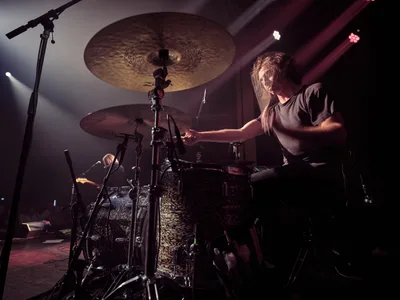 Drummer Julian Dorio of Band of Skulls unleashes rhythmic power behind his leopard-print kit during the band's 10 Year Anniversary Tour at Manhattan's historic Webster Hall. Stage lights carve dramatic shadows across his concentrated expression as he strikes cymbals suspended like bronze moons above the intricate hardware. The intimate venue's atmospheric lighting transforms the performance into a study of controlled intensity, capturing the percussive heartbeat that drives the English rock trio's decade-spanning catalog.