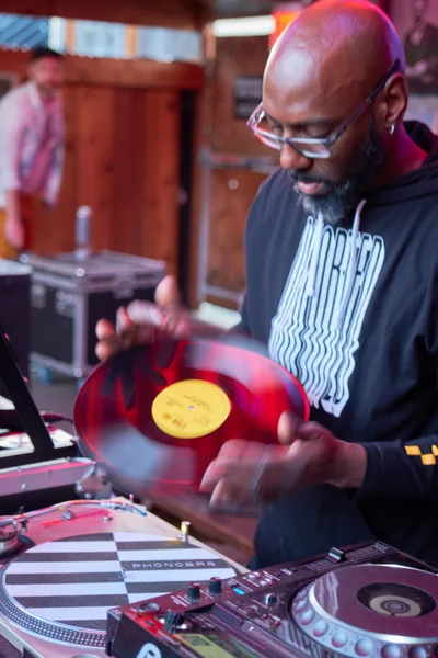 DJ Cee White commands the turntables at White Owl Social Club in Portland, his hands captured mid-motion as he manipulates a vibrant red vinyl record. The atmospheric lighting bathes the scene in warm amber and magenta hues, creating an intimate yet energetic ambiance typical of Portland's underground music venues. Motion blur on his hands emphasizes the kinetic energy of his performance, while the Pioneer DJ equipment gleams beneath the club's moody illumination. The photograph perfectly encapsulates the tactile artistry of vinyl DJing during this Sunday afternoon party opener.