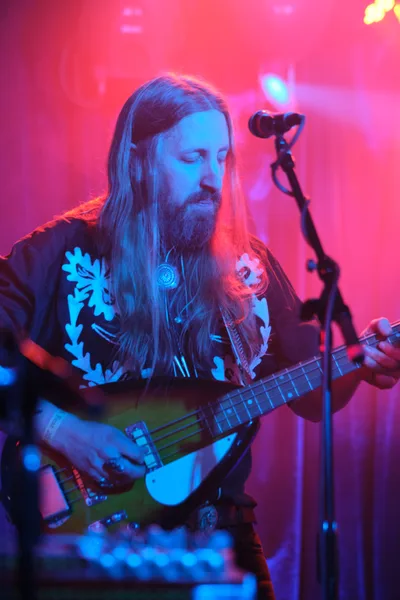 Tobias Berblinger of Roselit Bone lost in contemplative performance, his long blonde hair cascading as he cradles his bass guitar in the saturated magenta and blue stage lighting of Dante's. The intimate Portland venue's atmospheric haze creates a dreamlike backdrop, while ornate floral patterns on his dark shirt catch the vivid concert lighting. His downward gaze and gentle expression capture a moment of musical introspection during RX Fest 2019.