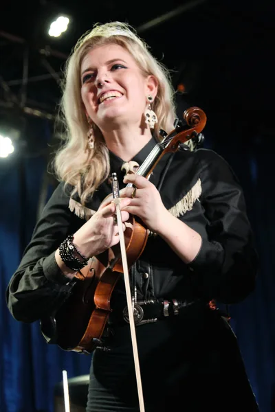 Faith Grossnicklaus of Roselit Bone delivers an electrifying violin performance at RX Fest 2019, her blonde hair catching the stage lights as she grins with pure musical joy. The intimate venue of Dante's in Portland creates a moody backdrop with its industrial ceiling and warm lighting, while her black leather jacket with fringe detail adds rock edge to the classical instrument. Her ornate earrings and studded bracelet gleam as she holds her violin with confident grace, embodying the perfect fusion of classical technique and alternative rock spirit.