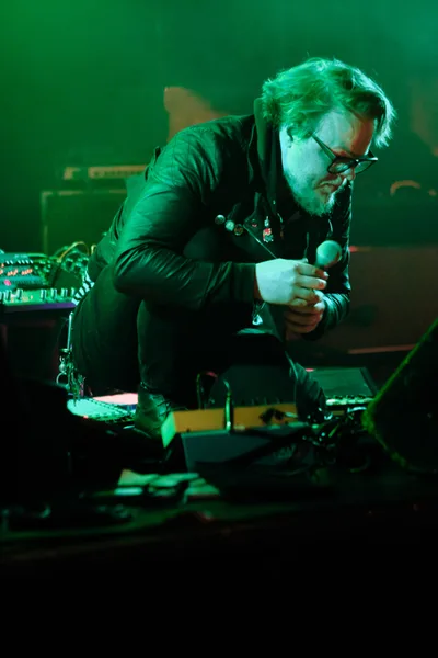 Electronic musician Eli Savage, performing as Ellipsism, leans into his microphone during an intense moment at RXFest 2019. Bathed in emerald stage lighting at Portland's iconic Dante's venue, the bearded performer clutches the mic while surrounded by synthesizers and electronic equipment. The atmospheric green glow creates a moody, underground ambiance that perfectly captures the raw energy of the electronic music scene.