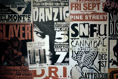 A dense collage of weathered concert promotional posters creates a visual archaeology of Portland's underground music culture. The overlapping flyers advertise performances by bands like Danzig, SNFU, and Cannibal at iconic venues including Pine Street Theatre and Satyricon. Muted earth tones and stark black-and-white graphics tell the story of the city's gritty alternative music heritage through torn paper and faded ink.
