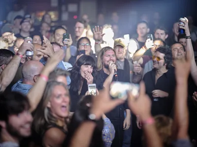 Emma Richardson and Russell Marsden of Band of Skulls are engulfed by an ecstatic crowd during their 10 Year Anniversary Tour at Manhattan's legendary Webster Hall. The intimate venue pulses with euphoric energy as fans raise smartphones and drinks toward the performers, creating a sea of illuminated faces bathed in atmospheric stage lighting. The smoky haze and tightly packed audience capture the raw intensity of live rock performance in one of New York's most storied music venues.