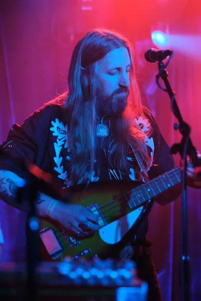 Tobias Berblinger of Roselit Bone surrenders to the sonic ritual beneath Dante's crimson-soaked stage lights in Portland. His flowing hair catches the electric blue and magenta wash as he cradles his bass guitar, eyes closed in musical meditation. The intimate venue pulses with atmospheric haze while his floral-printed shirt becomes a canvas for the club's signature neon palette. This moment captures the raw spirituality of underground performance, where musician and audience dissolve into pure sound.