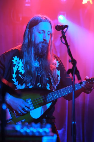 Tobias Berblinger of Roselit Bone commands the stage in a wash of electric blue and magenta lighting at RX Fest 2019. His long hair cascades over a floral-patterned shirt as he leans into his bass guitar, eyes closed in musical concentration. The intimate venue atmosphere is thick with colored stage lights cutting through atmospheric haze, creating a dreamlike quality that captures the raw energy of Portland's underground music scene.