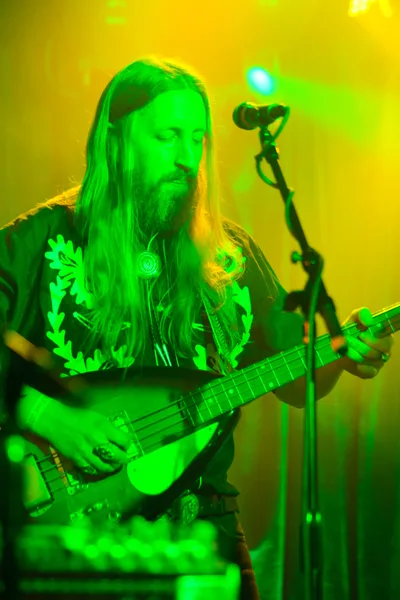 Tobias Berblinger of Roselit Bone commands the stage at Dante's in Portland, his silhouette bathed in otherworldly green stage lighting that transforms the intimate venue into a sonic cathedral. The bassist's flowing hair and concentrated expression are illuminated by the ethereal glow as atmospheric haze swirls through the performance space. His white bass guitar contrasts sharply against the verdant wash of light, while the microphone stand creates dramatic vertical lines that anchor the composition.