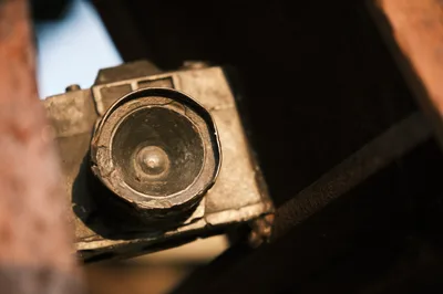 A weathered vintage camera lens rests in gentle hands within Portland's historic Skidmore district, its brass elements catching warm afternoon light. The intimate close-up reveals the circular glass element and aged metal housing, suggesting decades of photographic storytelling. Soft shadows and golden tones create an atmosphere of reverence for analog craftsmanship and photographic heritage.